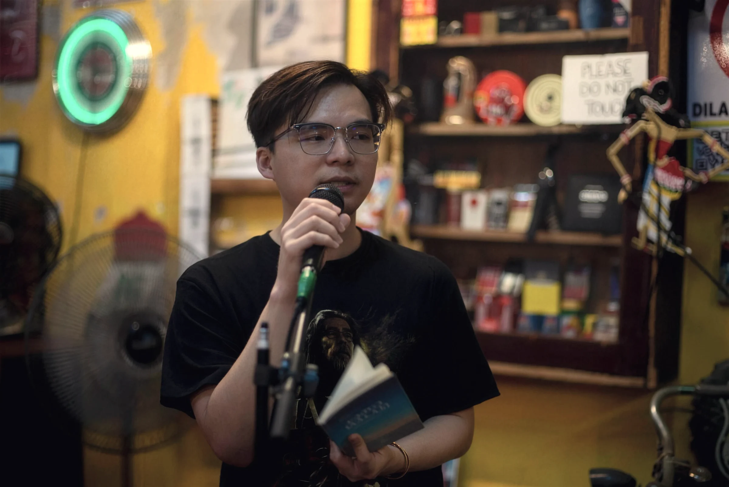 Lim Wei Wen membaca puisi daripada Pascamalam di hadapan mikrofon.